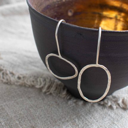 Mismatched oval shape pebble hook earrings by Sarah Drew hanging on a black beaker