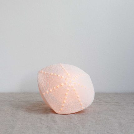 Porcelain lamp in the shape of a sea urchin, handcrafted by Amy Cooper Ceramics, lit up and sitting on a linen table cloth