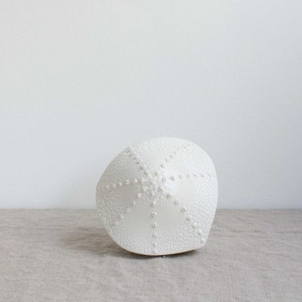 Porcelain lamp in the shape of a sea urchin, handcrafted by Amy Cooper Ceramics, sitting on a linen table cloth