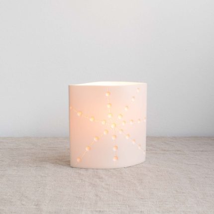 Porcelain ellipse lamp with starfish detail, handcrafted by Amy Cooper Ceramics, lit up and sitting on a linen table cloth