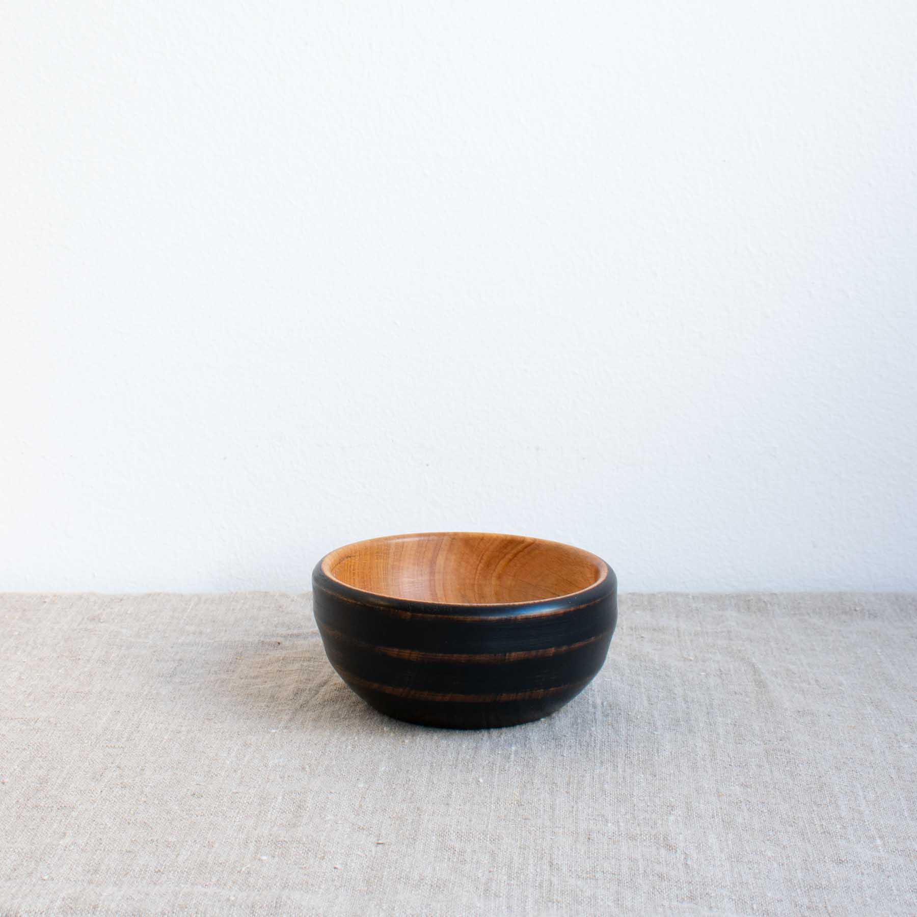 Small handcrafted wooden bowl finished on the outside with charcoal paint by The Hide Studio, sitting on a linen table cloth