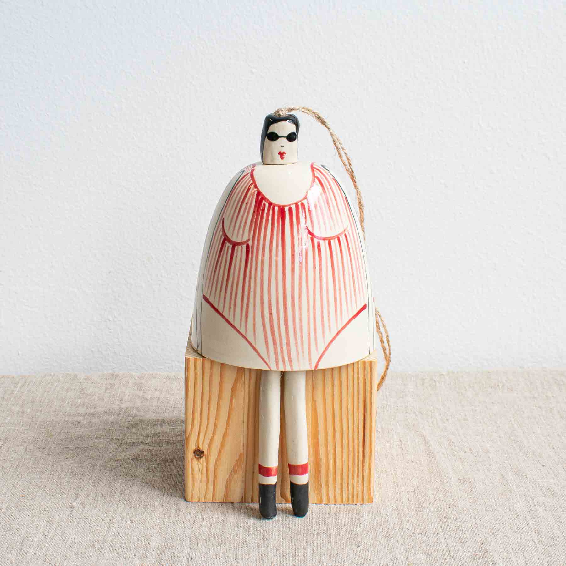 Handcrafted cream ceramic bell painted with a lady in red striped swimming costume, black hat and goggles by Lucie Sivicka, sitting on a linen table cloth