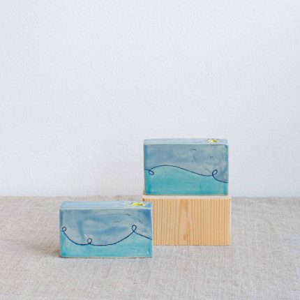 Pair of rectangular block stem vases decorated with a blue wave design and yellow sun around the opening, handcrafted by Michelle Foote, sitting on a linen table cloth