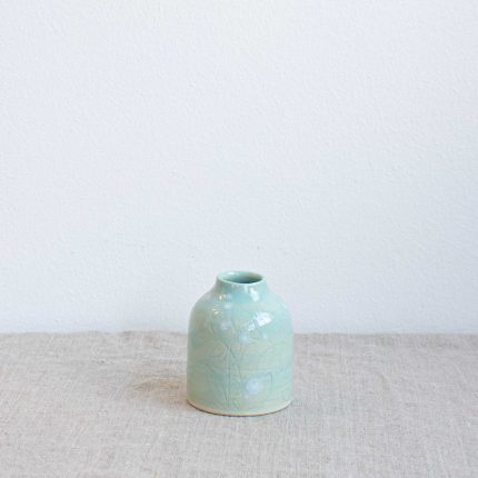 Ceramic bud vase with carved blossom detail and high shine green glaze finish, handcrafted by Michelle Foote, sitting on a linen table cloth