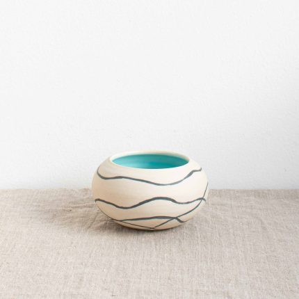 Ceramic pebble pot with matt white outside decorated with dark grey wavy lines and turquoise blue glazed inner, handcrafted by Michelle Foote, sitting on a linen table cloth