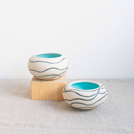 Two ceramic pebble pots with matt white outside decorated with dark grey wavy lines and turquoise blue glazed inner, handcrafted by Michelle Foote, sitting on a linen table cloth