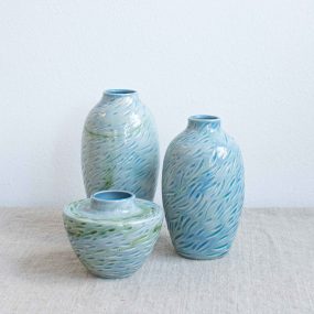 Group Of Ceramic Vases With Carved Design Resembling A Shoal Of Fish And Finished With A High Shine Pale Sea Blue Glaze, Handcrafted By Michelle Foote, Sitting On A Linen Table Cloth