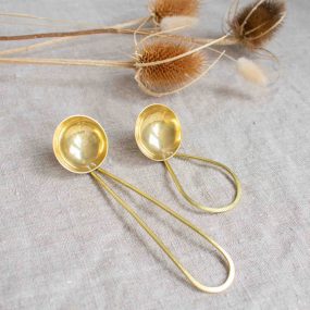 Two Brass Coffee Scoops Handcrafted By Razmaker On A Linen Tablecloth With Teasels