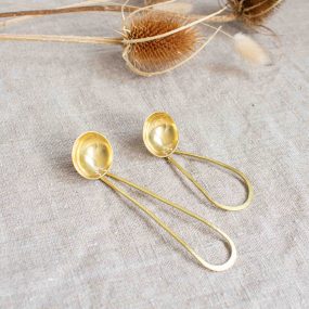 Two Brass Tea Scoops Handcrafted By Razmaker On A Linen Tablecloth With Teasels