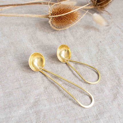 Two brass tea scoops handcrafted by Razmaker on a linen tablecloth with teasels