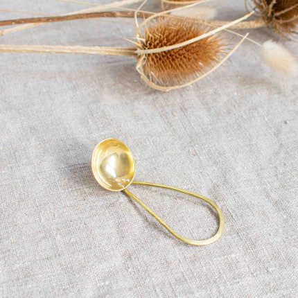 Short handled brass tea scoop handcrafted by Razmaker on a linen tablecloth with teasels