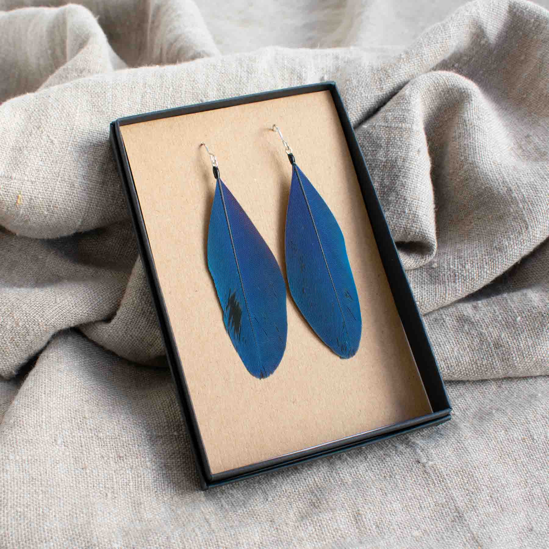 Pair of earrings made from blue feathers displayed in black box on linen by Saffron & Peach