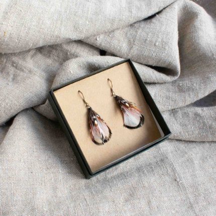 Pair of earrings made from white feathers displayed in black box on linen by Saffron & Peach