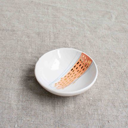 Small porcelain bowl with pink design and gold dots on a linen tablecloth by Frances Spice