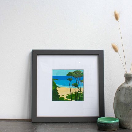 Painting of trees on the coast with blue sky in white mount and grey frame on table with vase by Karen Hemsley-Biggs