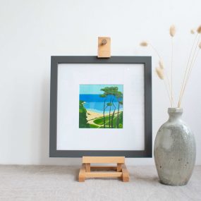 Painting Of Trees On The Coast With Blue Sky In White Mount And Grey Frame, On Easel On Linen Table Cloth With Vase By Karen Hemsley-Biggs