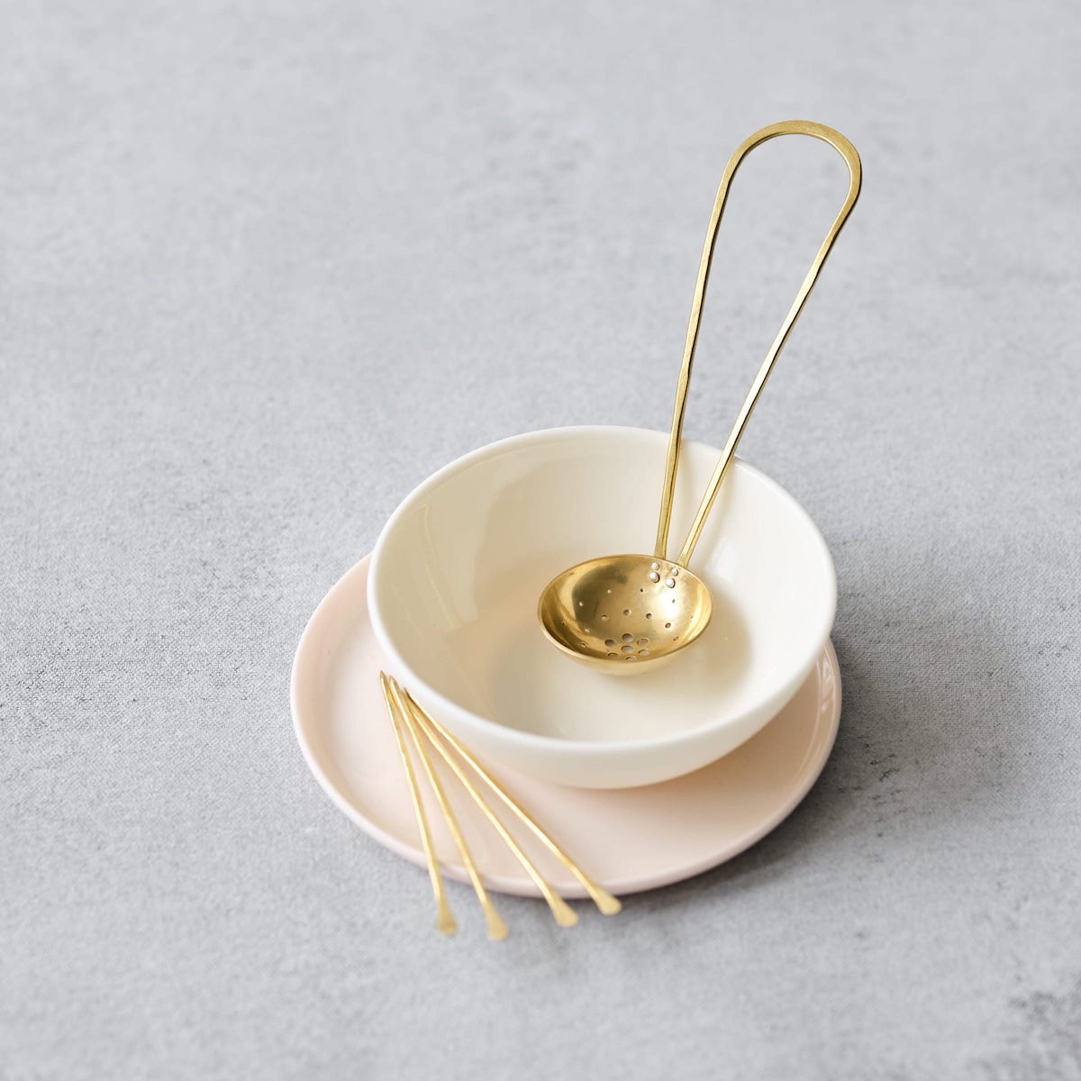 Long handled brass olive scoop in white porcelain and on pink plate with 4 brass olive picks by Razmaker