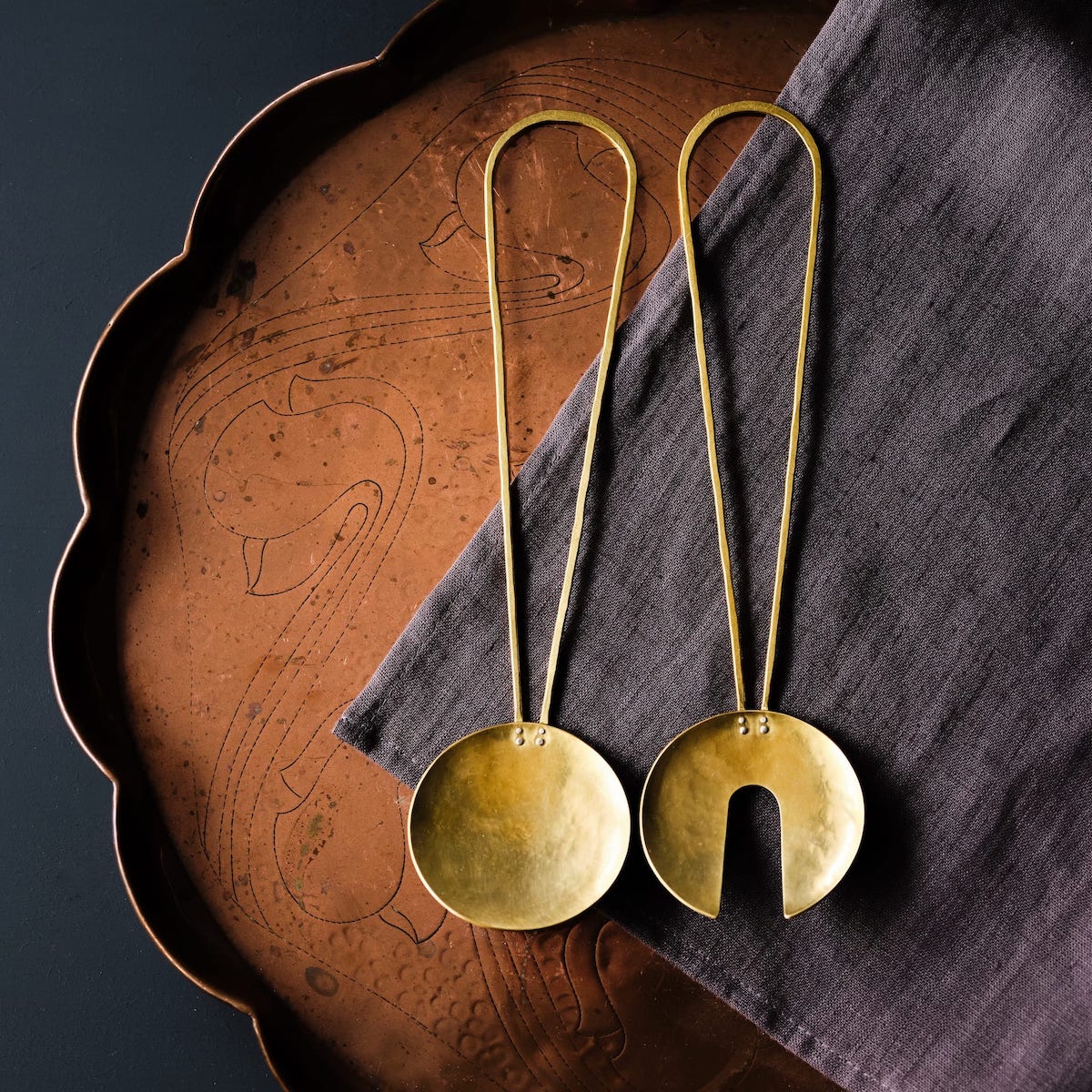 Pair of brass salt servers on a grey linen napkin and scalloped copper table by Razmaker