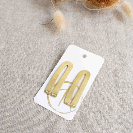 Pair of large brass stud earrings with silver dots which look like paws handcrafted by Razmaker on a linen tablecloth with teasels