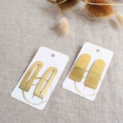 Two pairs of large brass stud earrings with silver dots which look like paws handcrafted by Razmaker on a linen tablecloth with teasels