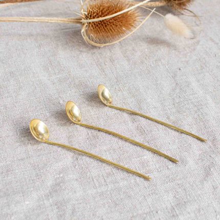 Trio of tiny brass salt spoons handcrafted by Razmaker on a linen tablecloth with teasels