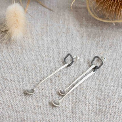 Silver long drop stud earrings in the shape of mini spoons handcrafted by Razmaker on a linen tablecloth with teasels