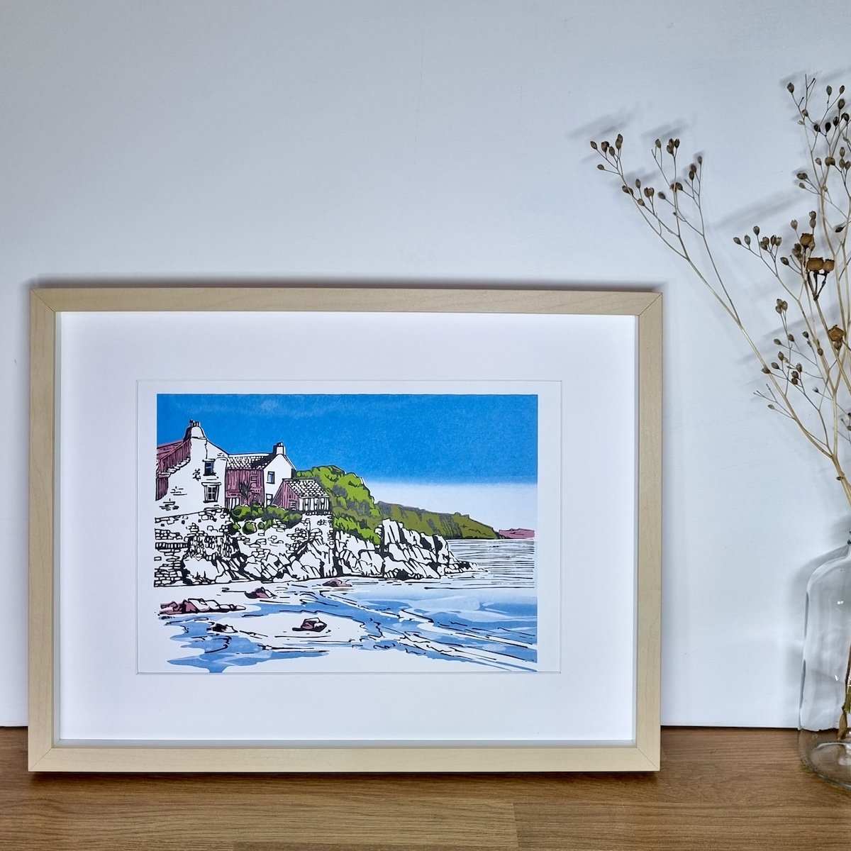 Wood framed picture of a coastal house on an oak table with vase